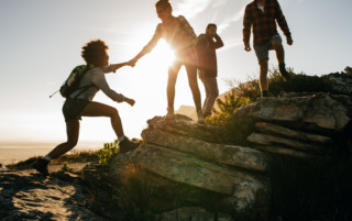 Young people on mountain hike at sunset Group of hikers on a mountain. Woman helping her friend to climb a rock. Young people on mountain hike at sunset.